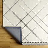 Close-up of the hand-tufted Holle Area Rug. Beige wool rug with a black geometric diamond pattern and a decorative border. Fold