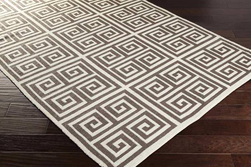 Close-up of the Hollytree Area Rug. Cream and dark red PVC rug with a contemporary geometric pattern on wood floors. Corner