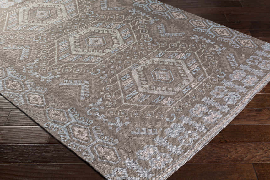 Close-up of Honeydew Area Rug. Hand-woven rug with cream, light gray, brown, and sky blue geometric pattern. Corner