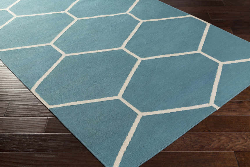 Close-up of Hoskins Area Carpet. Denim blue rug with off-white geometric pattern on dark wood floor. Corner