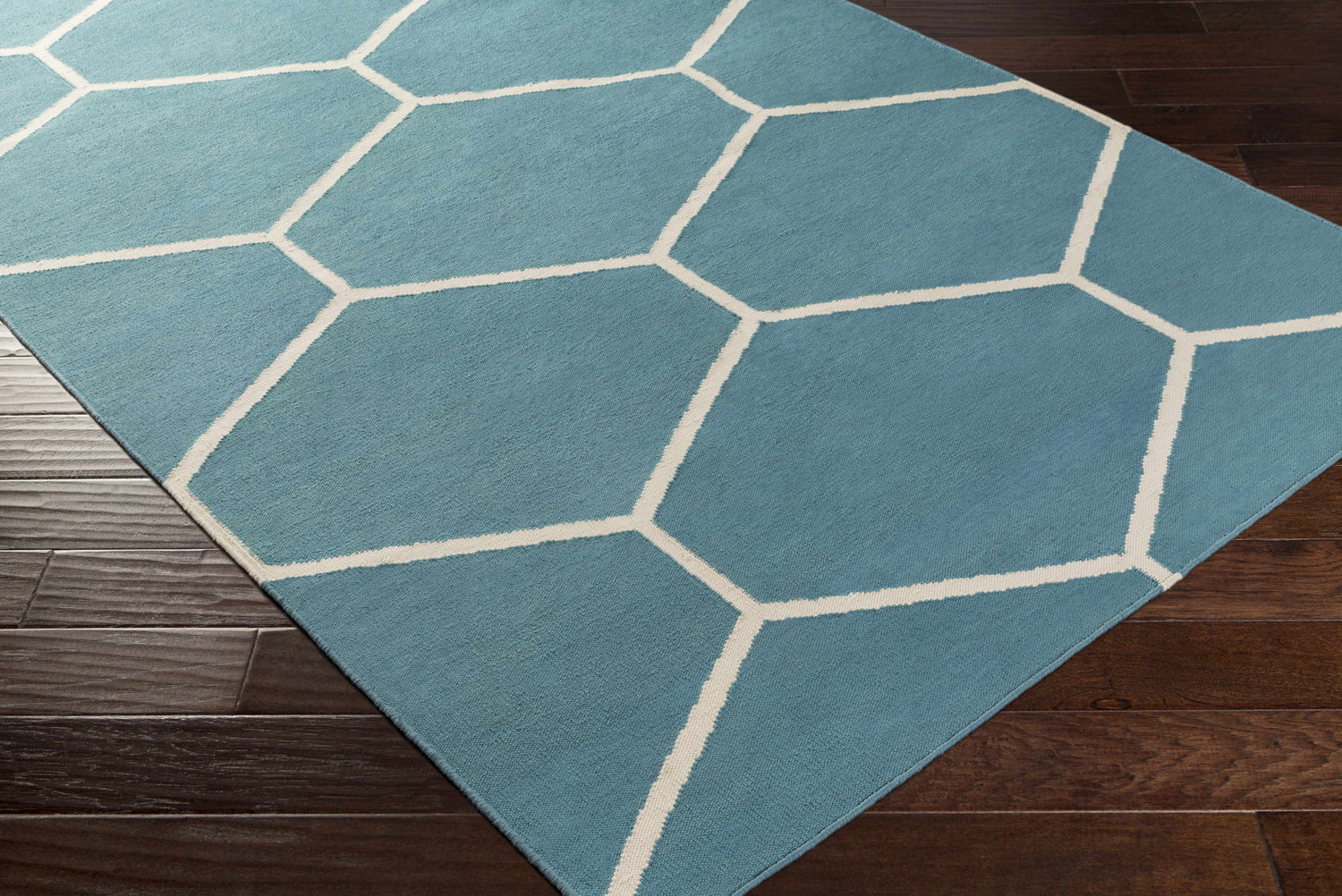 Close-up of Hoskins Area Carpet. Denim blue rug with off-white geometric pattern on dark wood floor. Corner