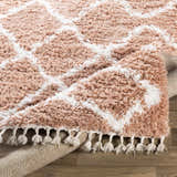 Close-up of the Hornsby Area Rug. Dusty pink shag rug with off white geometric pattern and tassels. Bohemian style. Fold