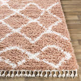 Close up of the Hornsby Area Rug, a dusty pink shag rug with off-white geometric pattern and tassels. Front