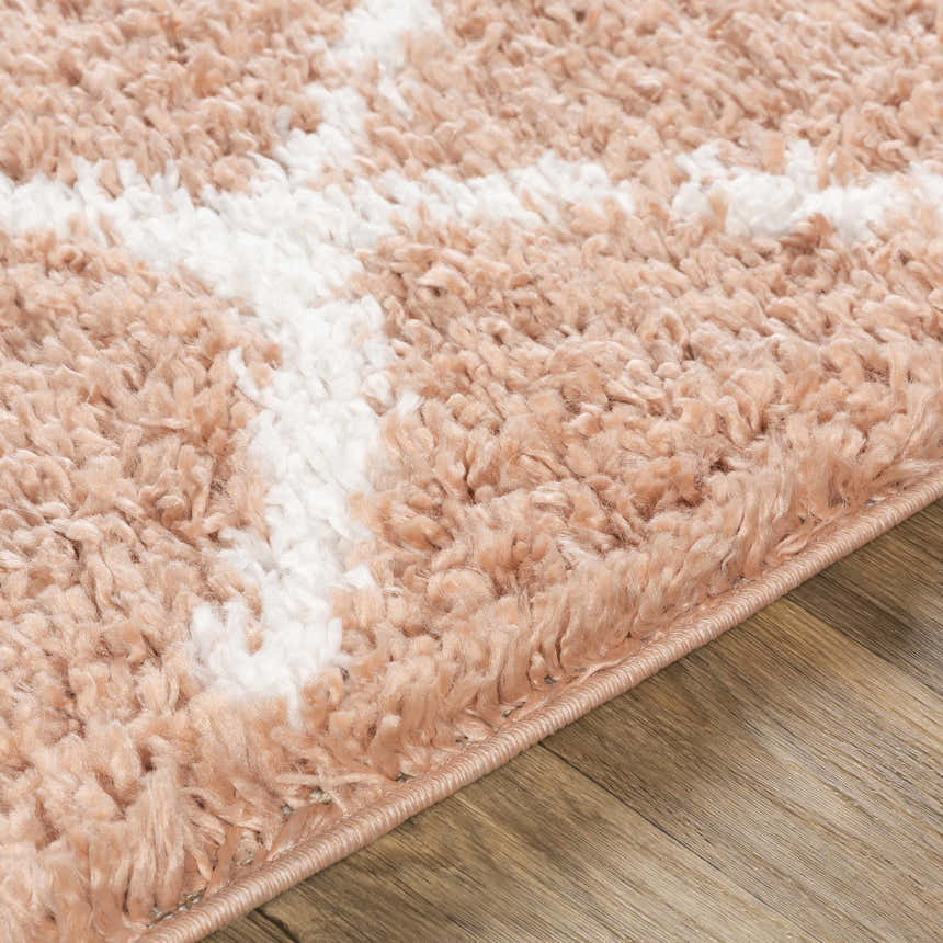 Close-up of the Hornsby Area Rug. Dusty pink and off-white shag rug with a geometric pattern on a wood floor. Texture