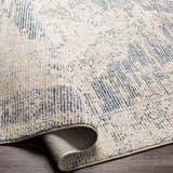 Close-up of the Herricks Denim Medallion Area Rug showing its cream, denim, and light beige colors and textured, woven design. Fold
