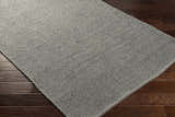 Close-up of the Innisfail Area Rug, a hand-woven rug in medium gray, showcasing its texture and construction on wood floors. Corner