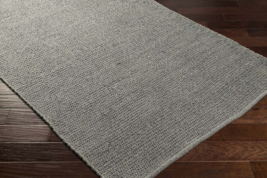 Close-up of the Innisfail Area Rug, a hand-woven rug in medium gray, showcasing its texture and construction on wood floors. Corner