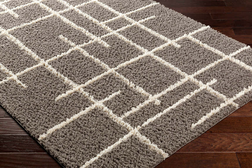 Close-up of a gray Isoke Area Rug with cream geometric shag design on a dark wood floor. Corner