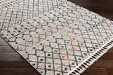 Close-up of Itogon Area Rug with geometric pattern in black, orange, blue, and brown on a light gray background. Tassels on the edge. Corner