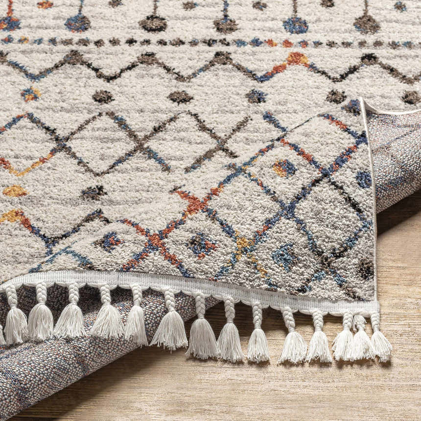 Close-up of the Itogon Area Rug, a geometric design in black, red, orange, brown, gray, and teal with white tassels. Fold