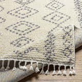 Close up of the Jabonga Area Rug showing its ivory shag texture, gray geometric pattern, and tassel fringe. Fold