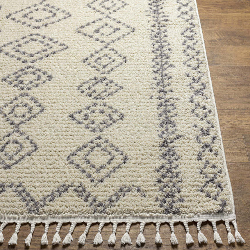 Close-up of the Jabonga Area Rug, a farmhouse style rug with a geometric gray pattern and tassels on a wood floor. Front