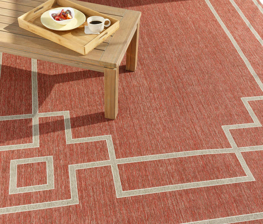 Brick red Jarrell Area Rug with light beige geometric pattern under a wood coffee table on a patio. Styleshot
