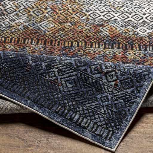 Close-up of the Joroan Area Carpet. Bohemian style rug with geometric patterns in white, orange, and navy blue. Fold