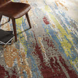 Close-up of the Kabugao Handmade Wool Rug with blue, red, beige, and gray abstract pattern and a modern wood chair. Styleshot