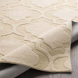 Close-up of the tan Kake Carpet, a hand-loomed wool rug with a contemporary quatrefoil pattern. Neutral texture. Fold