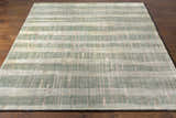 Close-up of the Kalaheo Premium Rug. Sage green wool rug with a contemporary striped pattern on a hardwood floor. Front