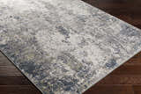 Close-up of the Kanahooka Area Rug, a contemporary rug in charcoal, beige, and blue, on a dark wood floor. Corner