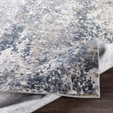 Close-up of the Kanahooka Area Rug with charcoal, dark blue, light beige, and gray abstract pattern and machine woven texture. Fold