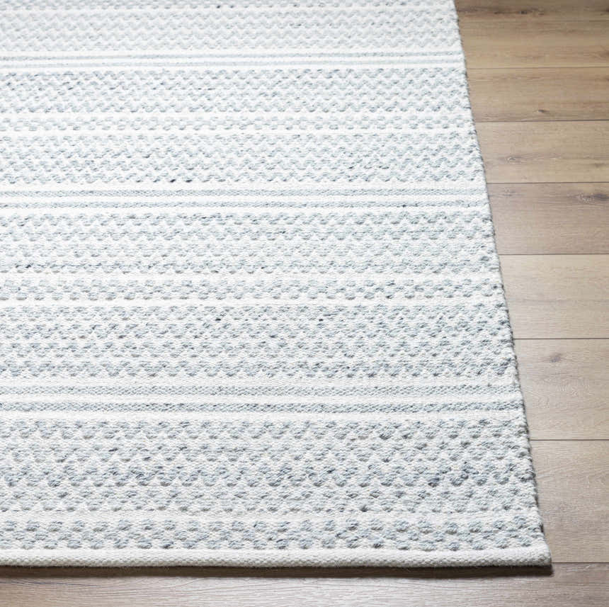 Close-up of the hand woven Kendi Cream Area Rug showing its cream and light slate textured pattern on wood floor. Front