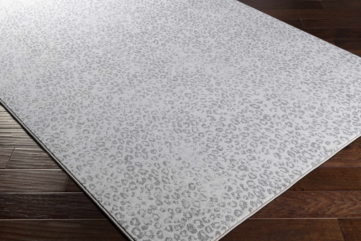 Close-up of the Keenes Leopard Print Area Rug in charcoal and cream on a dark wood floor. Contemporary animal print rug. Corner