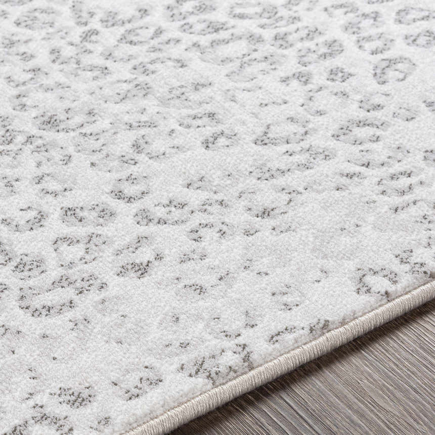 Close-up of the Keenes Leopard Print Area Rug showing charcoal spots on a cream and light gray textured surface. Texture