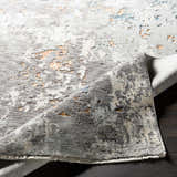Close-up of the Kenedy Carved Statement Carpet, showcasing its gray, ivory, blue, and orange contemporary design and textured weave. Fold