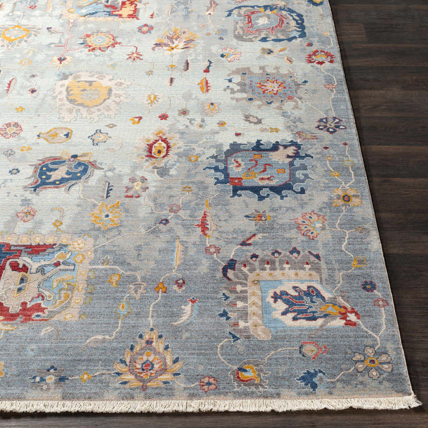Close-up of the Kernersville Area Rug showing its blue, burnt orange, and gray traditional floral pattern and fringe. Front