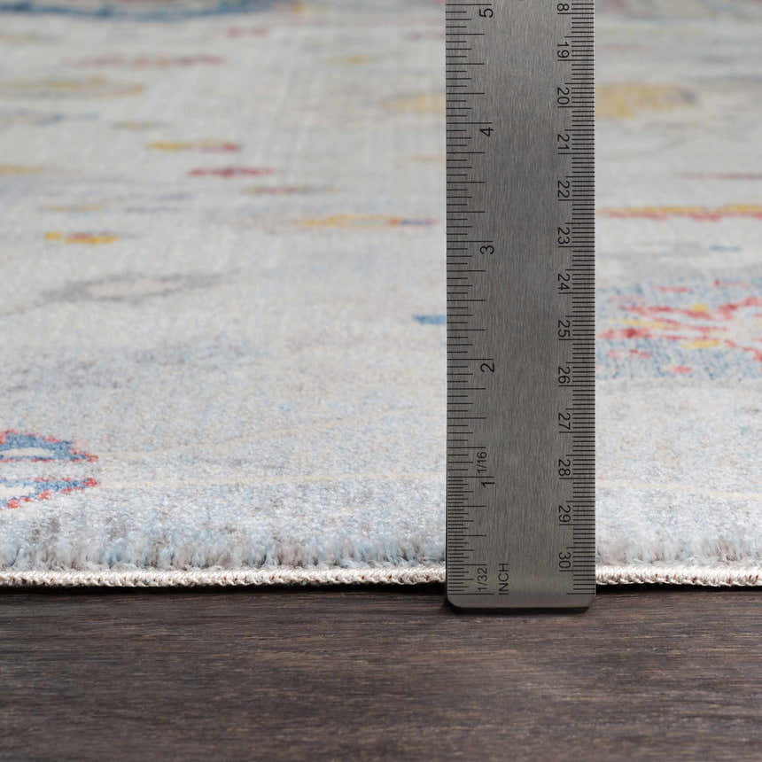Close up of Kernersville Area Rug showing light beige, blue, and rose colors. Ruler shows rug thickness. Pile