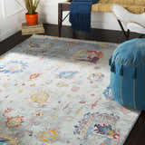 Bohemian room scene with Kernersville Area Rug in blue, orange, and gray. Features a bench, chair, and blue pouf. Roomscene-Rectangle