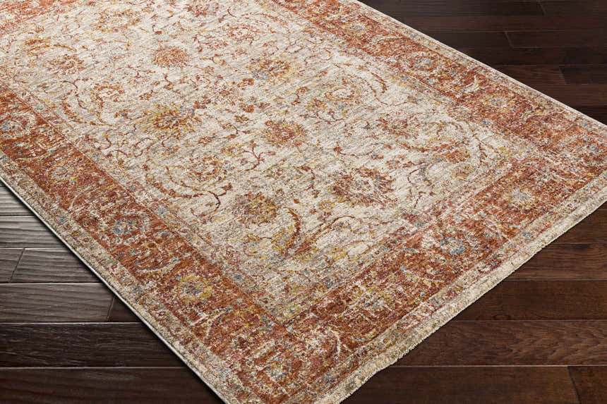 Kilsby Area Rug on dark wood floor. Traditional floral pattern in rust, beige, gold, and blue. Machine woven rug. Corner