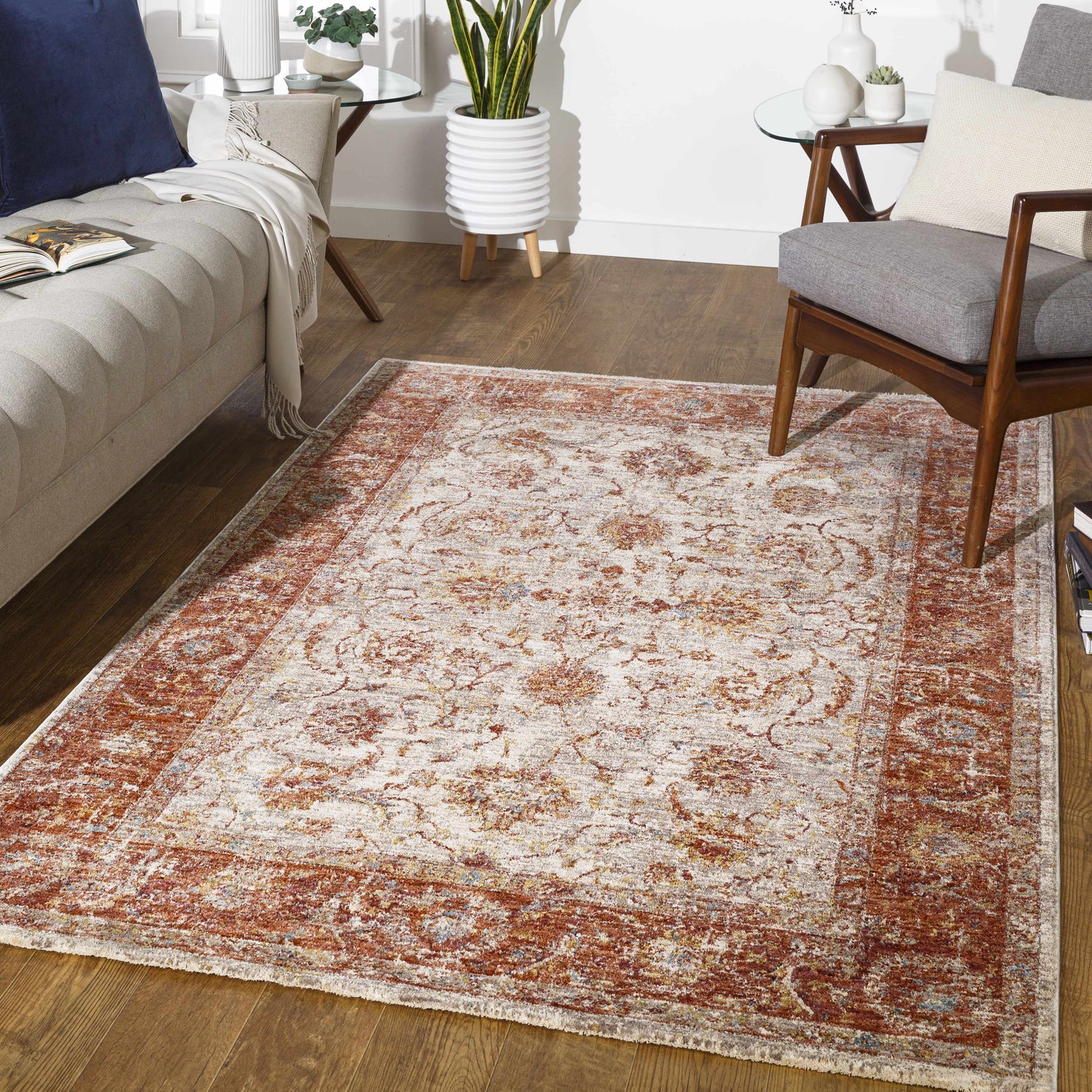 Living room scene with a Kilsby Area Rug, beige sofa, wood chair, and plants creating a cozy, contemporary space. Roomscene-Rectangle