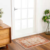Entryway scene with a Kilsby Area Rug. The rug has a traditional orange and cream pattern. Modern wood dresser and white door. Roomscene-Rectangle