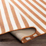 Close-up of the Kington Area Rug showing a striped pattern in brick red and cream on a dark wood floor. Fold