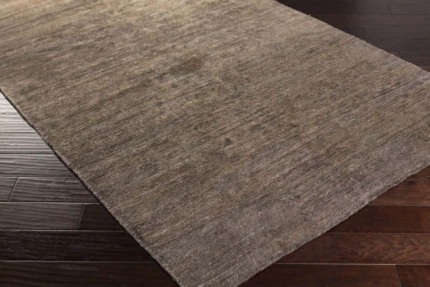 Close-up of the hand-woven Kingwood Area Rug. Dark and light brown viscose rug with subtle texture on dark wood flooring. Corner