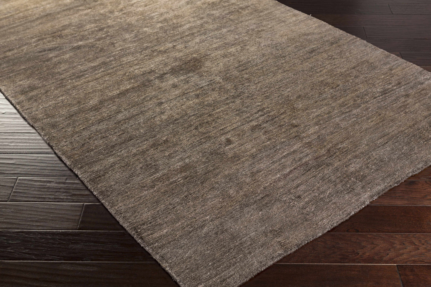 Close-up of the hand-woven Kingwood Area Rug. Dark and light brown viscose rug with subtle texture on dark wood flooring. Corner