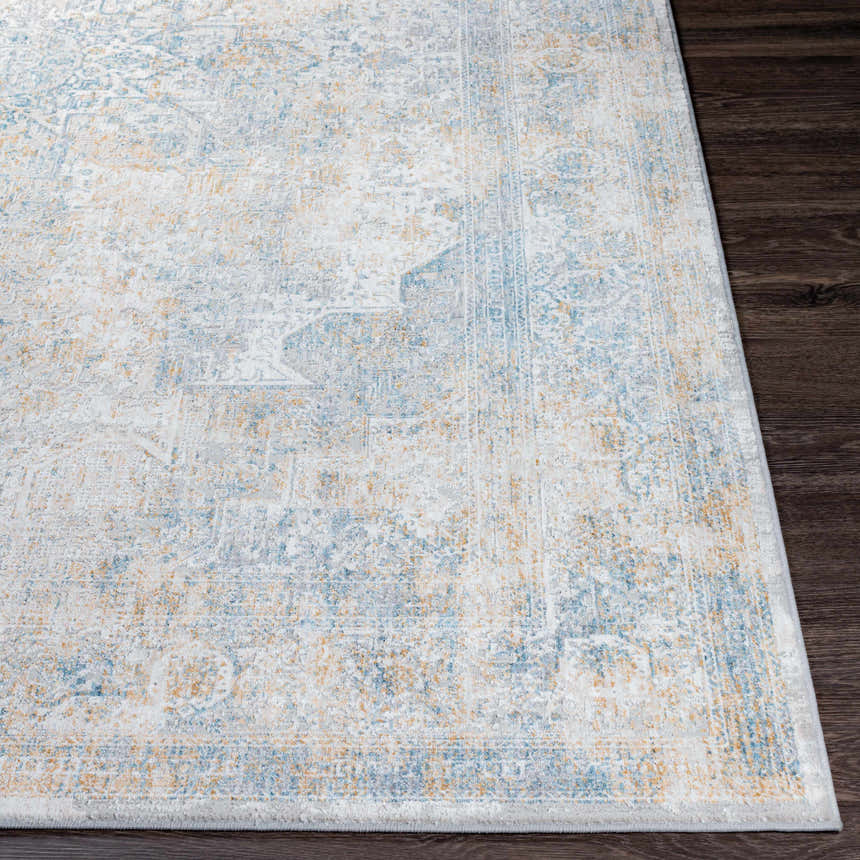 Close-up of the Kintbury Area Rug. Bohemian style rug with blue, mustard, and off-white hues on a dark wood floor. Front