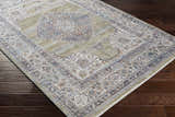 Close-up of Klahanie Area Carpet on dark wood floor. Bohemian style rug with brick red, cream, blue, and gray oriental pattern. Corner