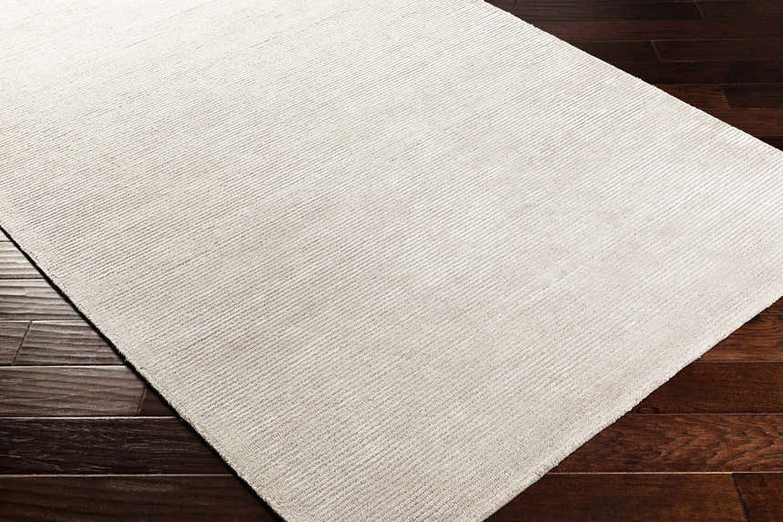 Close-up of light gray Keller Area Rug with subtle stripes, hand-tufted texture, and dark wood floor. Corner