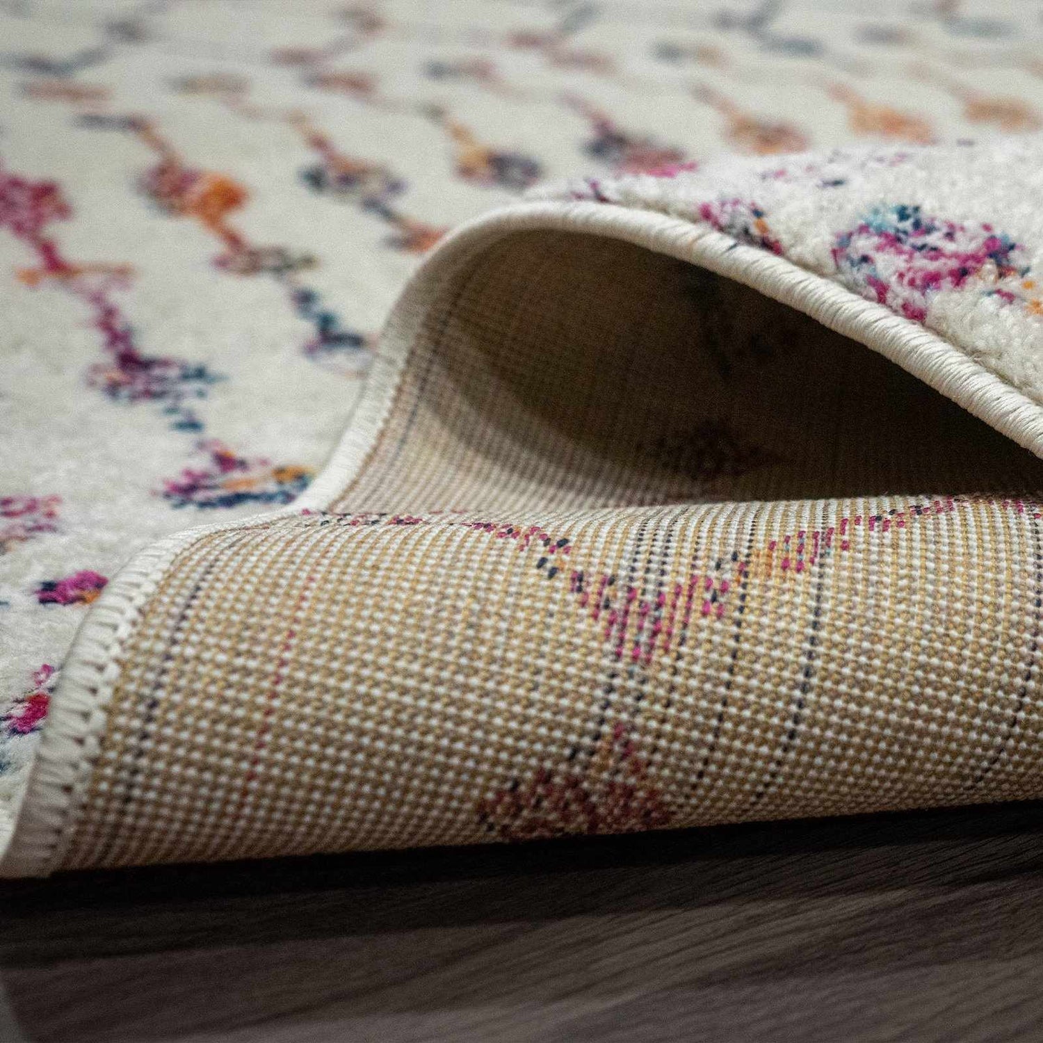 Close-up of the Marash KMRSH-4600 area rug showing its off-white base with colorful bohemian pattern and the rug's backing. Fold