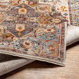 Close-up of the Kokstad Area Rug. Features an intricate oriental pattern in arctic stone, beige, brown, mocha, and taupe. Fold