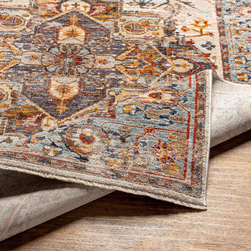 Close-up of the Kokstad Area Rug. Features an intricate oriental pattern in arctic stone, beige, brown, mocha, and taupe. Fold