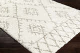 Close-up of the ivory Kunia Area Rug, featuring a geometric shag design on dark wood flooring. Corner