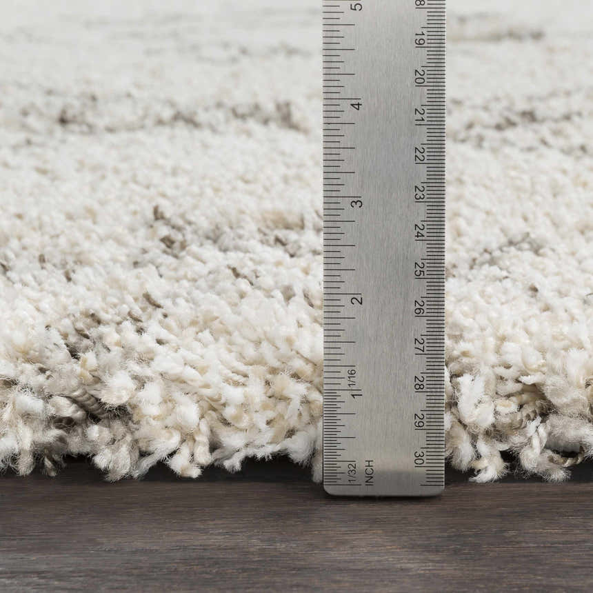 Close up of the Kunia Area Rug showing the shag texture and pile height with a ruler. Colors: ivory, taupe. Pile