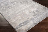 Close-up of the textured Kyabram Area Rug. Abstract design in beige, charcoal, gray, medium brown, and off-white. Corner