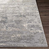 Close-up of the textured Kyabram Area Rug showing beige, charcoal, gray, and off-white abstract design on dark wood floor. Front
