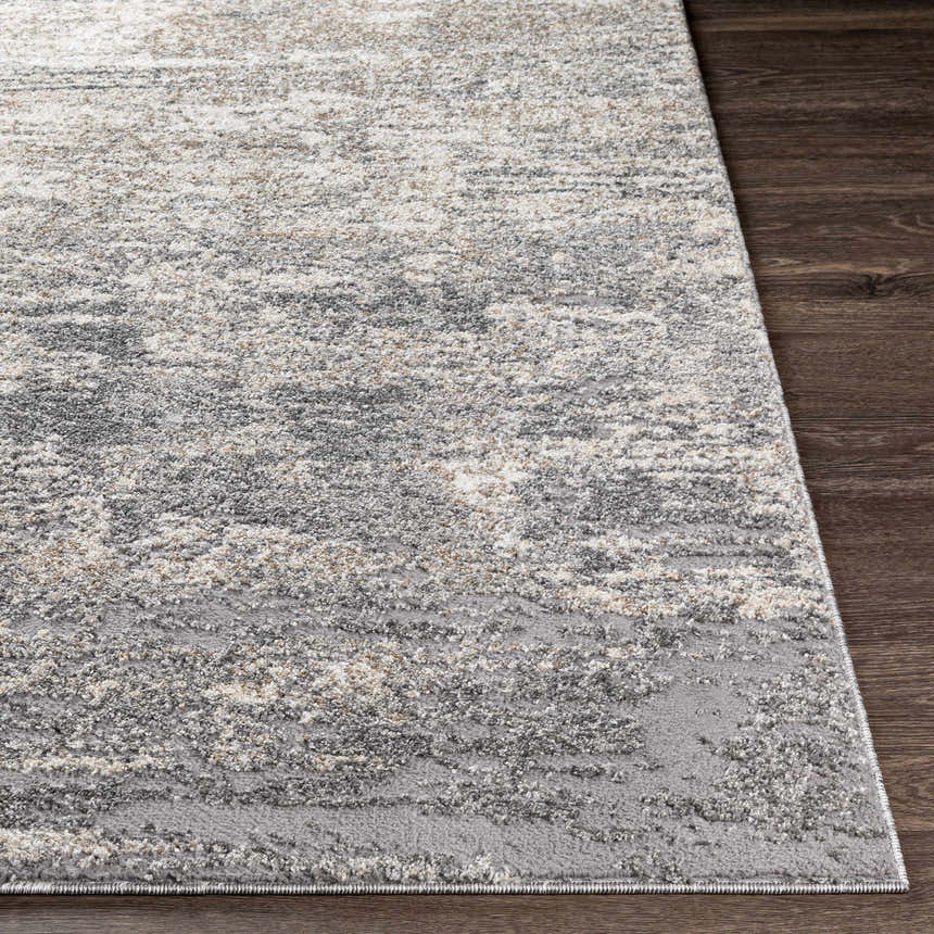 Close-up of the textured Kyabram Area Rug showing beige, charcoal, gray, and off-white abstract design on dark wood floor. Front
