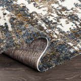 Close-up of the Lafontaine Boutique Area Rug showing its cream, blue, brown, and mustard abstract pattern and shag texture. Fold