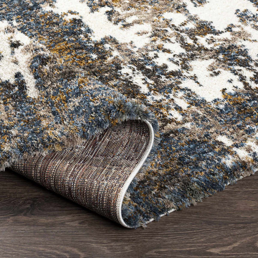 Close-up of the Lafontaine Boutique Area Rug showing its cream, blue, brown, and mustard abstract pattern and shag texture. Fold