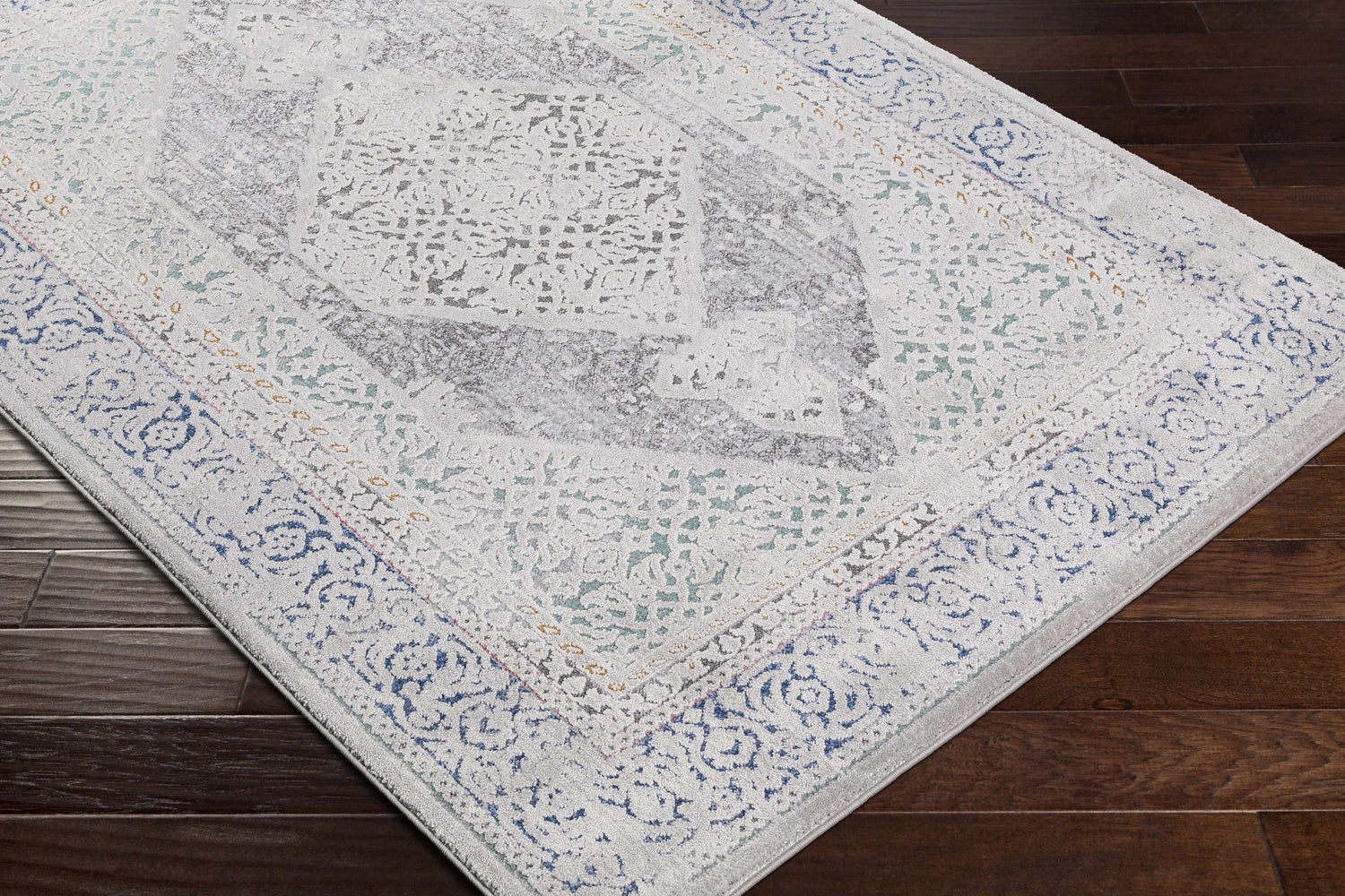 Close-up of the Laplace Area Rug showing its vintage-inspired design, blue, charcoal, and gray tones on a dark wood floor. Corner